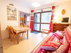 Une pièce confortable avec une table à manger, des chaises, un canapé, un téléviseur et une fenêtre avec des rideaux.
