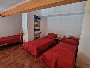 Habitació amb dos llits individuals, una escala de fusta, una prestatgeria amb roba doblegada i un biga de sostre de fusta.