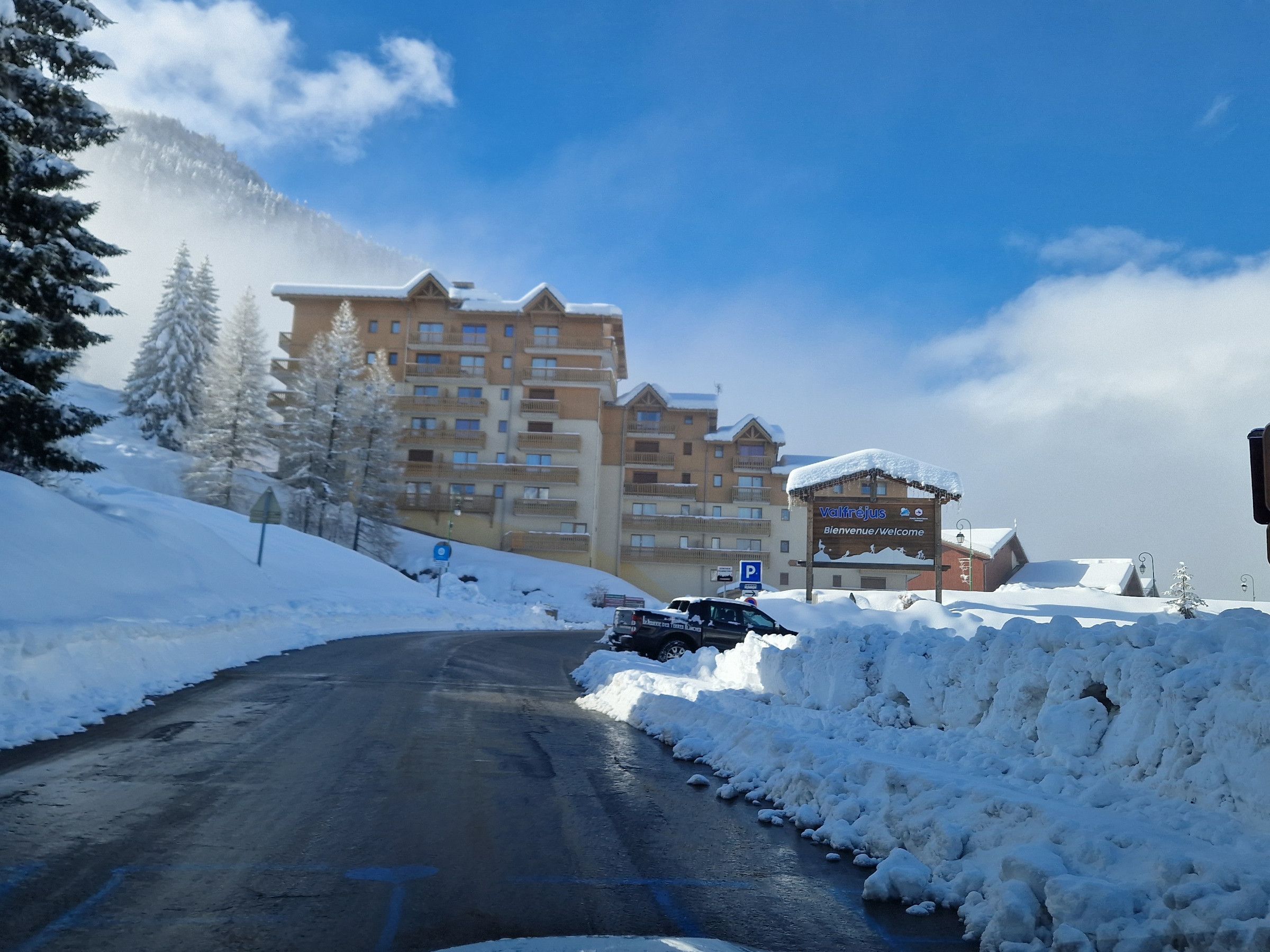 A snow-covered road leading to a multi-story building with a sign reading 'Bienvenue/Welcome.'
