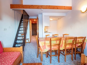 A dining area with a table set for four, wooden chairs, a red sofa, and a staircase leading to an upper level. - Quiet apartment by the forest - 4/6 guests (Villarodin-Bourget)