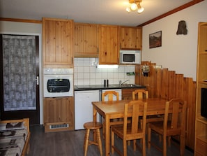 A compact kitchen with wooden cabinets, a microwave, a stove, and a sink. - Quiet apartment, forest - 4 guests (Villarodin-Bourget)