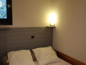 A bedroom with a bed, pillows, a nightstand, a wall-mounted light, and a window with a view of trees. - Quiet apartment, forest - 4 guests (Villarodin-Bourget)