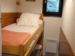 A single wooden bed with a white mattress and a peach-colored blanket, a white wall with a window, and a white radiator. - Quiet apartment, forest - 4 guests (Villarodin-Bourget)