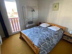 A single bed with a geometric patterned bedspread, a wooden headboard, a bedside table with a lamp, a hanging clothes rack, and a window with a view of a balcony. - Practical studio, balcony & chalet view - 8 guests (Arette)