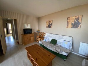 A living room with a sofa, a wooden coffee table, a television on a wooden cabinet, and two wall-mounted paintings. - Practical studio, balcony & chalet view - 8 guests (Arette)
