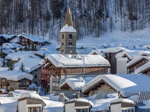 A snow-covered village with traditional wooden buildings, a church with a bell tower, and a ski slope in the background. - Luxury apartment with parking - 6 guests (Val-d'Isère)