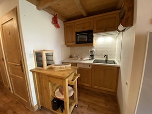 A compact kitchen with wooden cabinets, a microwave, a coffee maker, and a small wooden table with a basket and a plate. - Cozy mountain apartment - 4 guests (Arêches-Beaufort)