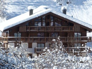 A multi-story wooden chalet with balconies, surrounded by snow-covered trees. - Cozy mountain apartment - 4 guests (Arêches-Beaufort)