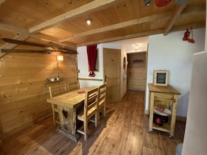 A wooden interior with a dining table and chairs, a small kitchen area, and a door leading to another room. - Cozy mountain apartment - 4 guests (Arêches-Beaufort)