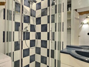 A bathroom with a checkered tile wall, a glass shower enclosure, a black countertop, and a white sink. - Charming south-facing studio - 3/4 guests (La Plagne)