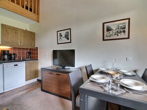 A dining area with a table set for four, a television, and kitchen cabinets in the background. - Charming duplex, slopes view - 4 guests (Belle Plagne)