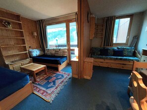 A compact room with a bed, a small table, a bench, and a window with a view of trees. - Bright studio at the foot of the slopes (Valmorel)