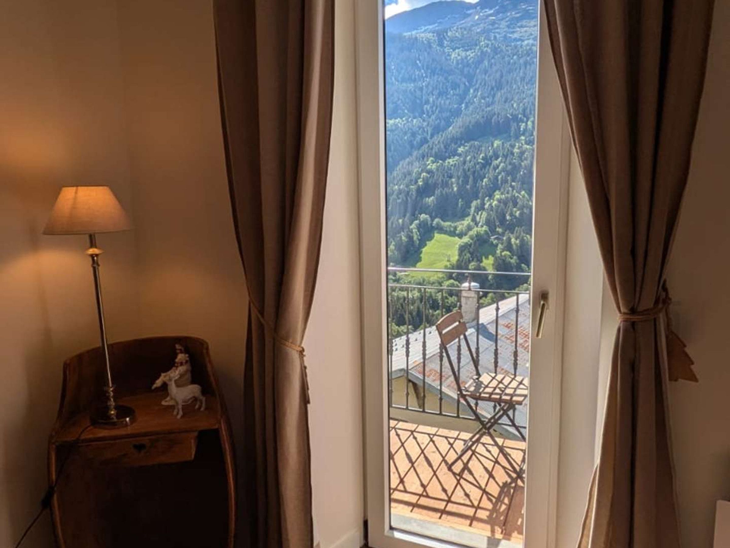 Una habitación con vistas a un paisaje montañoso, visible a través de una ventana con cortinas.