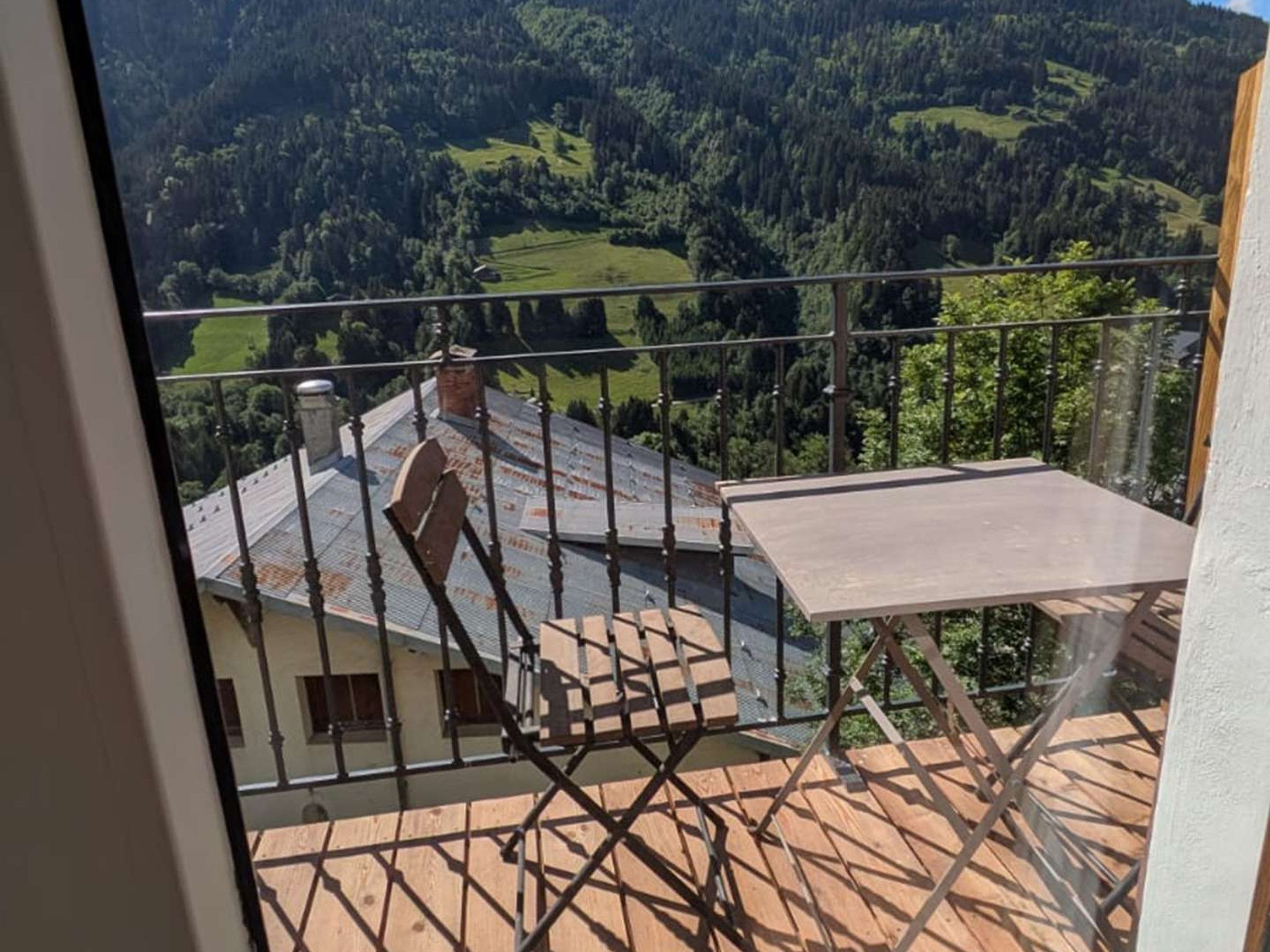 Un balcón con vistas a un valle boscoso, una mesa de madera y una barandilla de metal.