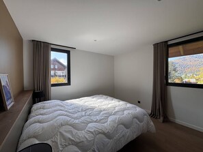 A bedroom with a large bed, two windows, and a view of a house and mountains. - Modern house in village center - 12 guests (Villard-de-Lans)