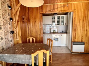 A wooden interior with a dining table, chairs, a washing machine, and a small kitchen area. - 2-room apartment by the slopes - 4 guests (Huez)