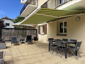 Een terras met een tafel en stoelen, een overdekte zithoek en uitzicht op een naburig gebouw.
