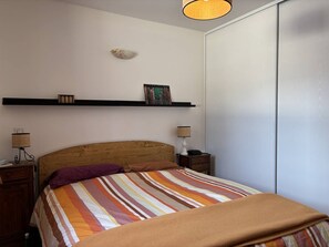A bedroom with a wooden headboard, a striped bedspread, two bedside lamps, a shelf with decorative items, and a wardrobe. - Apartment with wifi - 6 guests, mountain view (Villard-de-Lans)