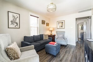 Un salon avec un canapé gris, un pouf bleu, un fauteuil gris et une lampe posée sur une table d’appoint.