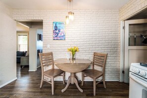 A dining area with a brick wall, two wooden chairs, a round table, and a vase with yellow flowers. - #StayInMyDistrict 2Bed DogsOk Spa Monthly Rental (Boise)