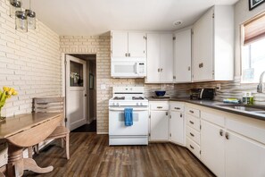 A kitchen with white cabinets, a stove, a microwave, and a wooden dining table with a bench. - #StayInMyDistrict 2Bed DogsOk Spa Monthly Rental (Boise)