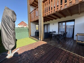 Eine Holzterrasse mit Außenmöbeln, einem überdachten Tisch und einem überdachten Grillbereich.