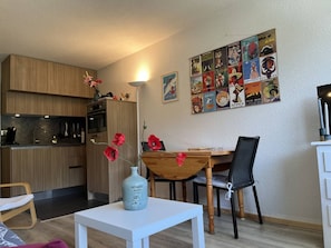 A modern kitchen with wooden cabinets, a dining table with chairs, and a vase with red flowers on a small table. - Comfortable studio with balcony - 4 guests (Villard-de-Lans)