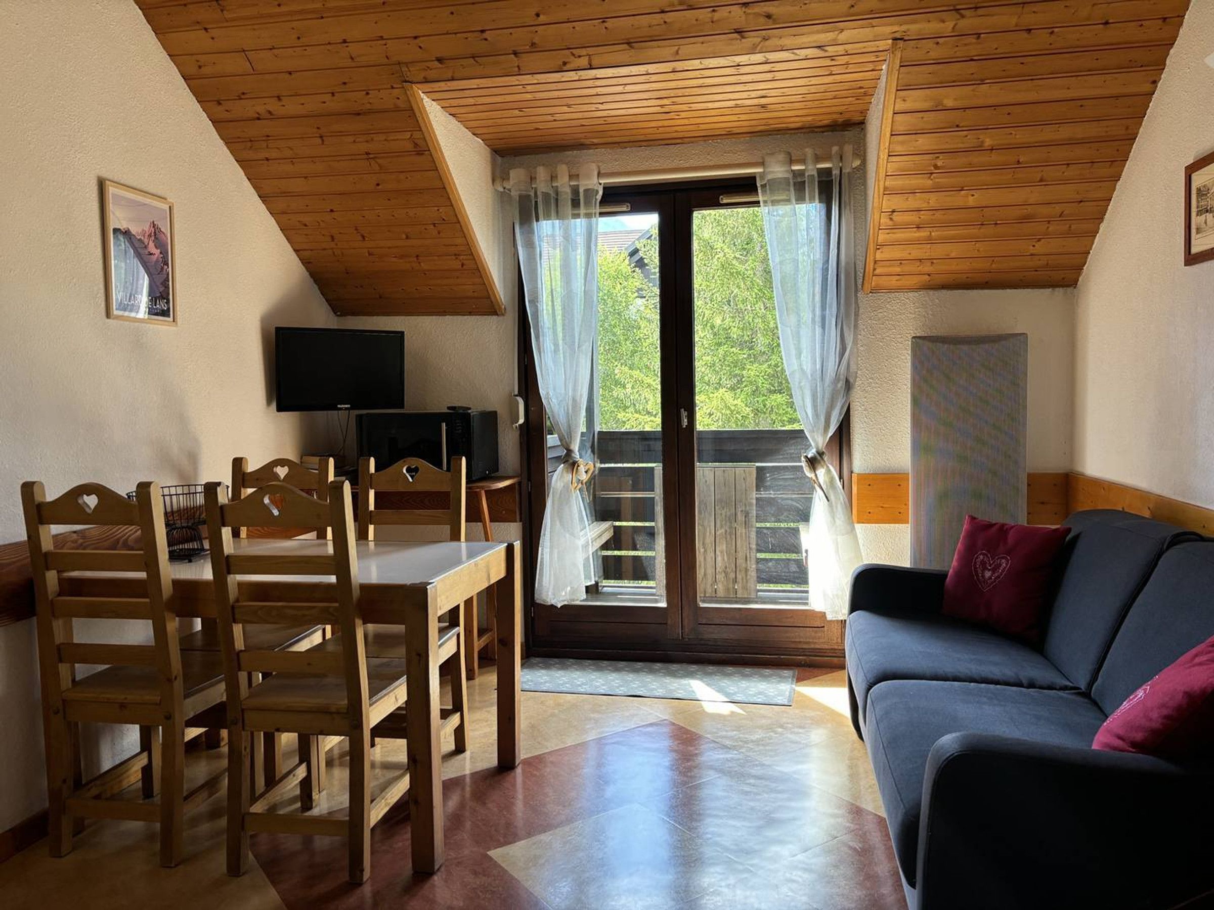 Una habitación acogedora con techo de madera, una mesa de comedor con sillas, un sofá y un televisor en la pared.