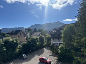 A parking lot with a red car, surrounded by trees and buildings with a mountain in the background. - Cozy studio in the heart of the village - 2 guests (Villard-de-Lans)