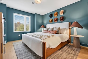 A bedroom with a bed, two bedside lamps, a window with blinds, and a wall with decorative plates. - Garage, Near Downtown Broadway + Rooftop with Dining Table (Nashville)