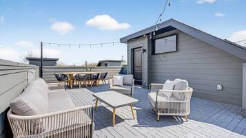 A rooftop patio with outdoor furniture, a small building, and string lights.