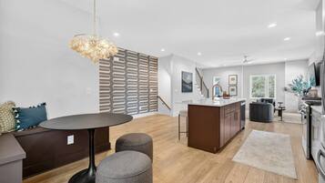 A modern kitchen with a central island, a dining area with a round table, and a seating area with a sofa and ottomans.