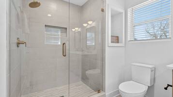 A modern bathroom with a glass-enclosed shower, a toilet, and a window with blinds.