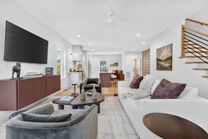 A modern living room with a flat-screen TV, a sofa, a coffee table, and a dining area in the background. - Garage, Near Downtown Broadway + Rooftop with Dining Table (Nashville)