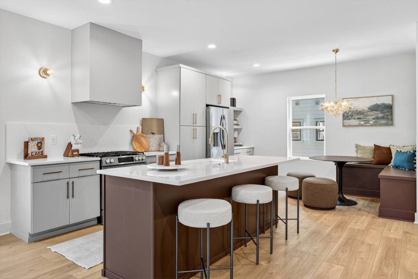 A modern kitchen with a central island, bar stools, and a dining area with a view.