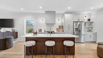 A modern kitchen with a central island, bar stools, stainless steel appliances, and a flat-screen TV.