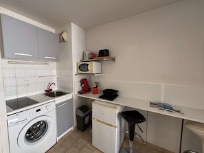 Eine kompakte Küche mit Waschmaschine, Mikrowelle und Kaffeemaschine.