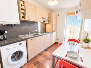A compact kitchen with a washing machine, a sink, and a dining area with a table and chairs. - Spacious apartment, sea view - 4 guests (Canet-en-Roussillon)