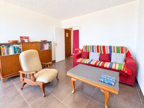 A living room with a wooden chair, a red sofa, a bookshelf, and a coffee table. - Spacious apartment, sea view - 4 guests (Canet-en-Roussillon)