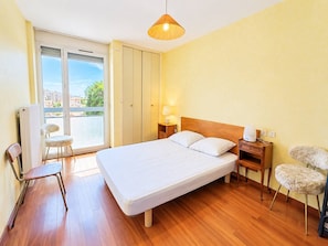 A hotel room with a bed, a chair, a nightstand, a lamp, and a view through a sliding door. - Spacious apartment, sea view - 4 guests (Canet-en-Roussillon)