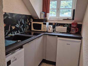 Ett kompakt kök med mikrovågsugn, kaffebryggare och diskmaskin.