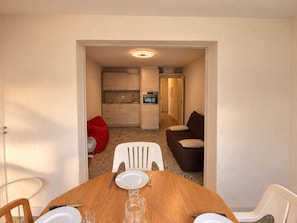 A dining area with a wooden table, white chairs, and a brown sofa in the background. - Ideal apartment in Six-Fours - 4 guests (Six-Fours-les-Plages)