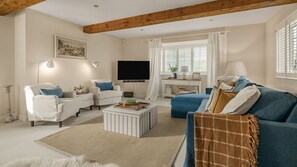 Ein Wohnzimmer mit einer Couch, Sesseln, einem Couchtisch, einem Fernseher und einem Fenster mit Jalousien.