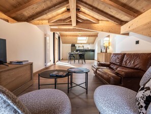 Ein geräumiger Wohnbereich mit hoher Decke, Holzbalken, einem Ledersofa, einem Couchtisch und einem Fernseher.