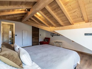 Ein Schlafzimmer mit einem großen Bett, einer Holzbalkendecke, einem roten Stuhl und einer weißen Wand.