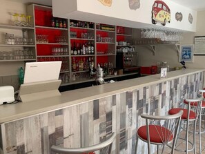 Eine Bar mit Regalen voller Flaschen und Gläsern, einer Kasse und roten Barhocker.