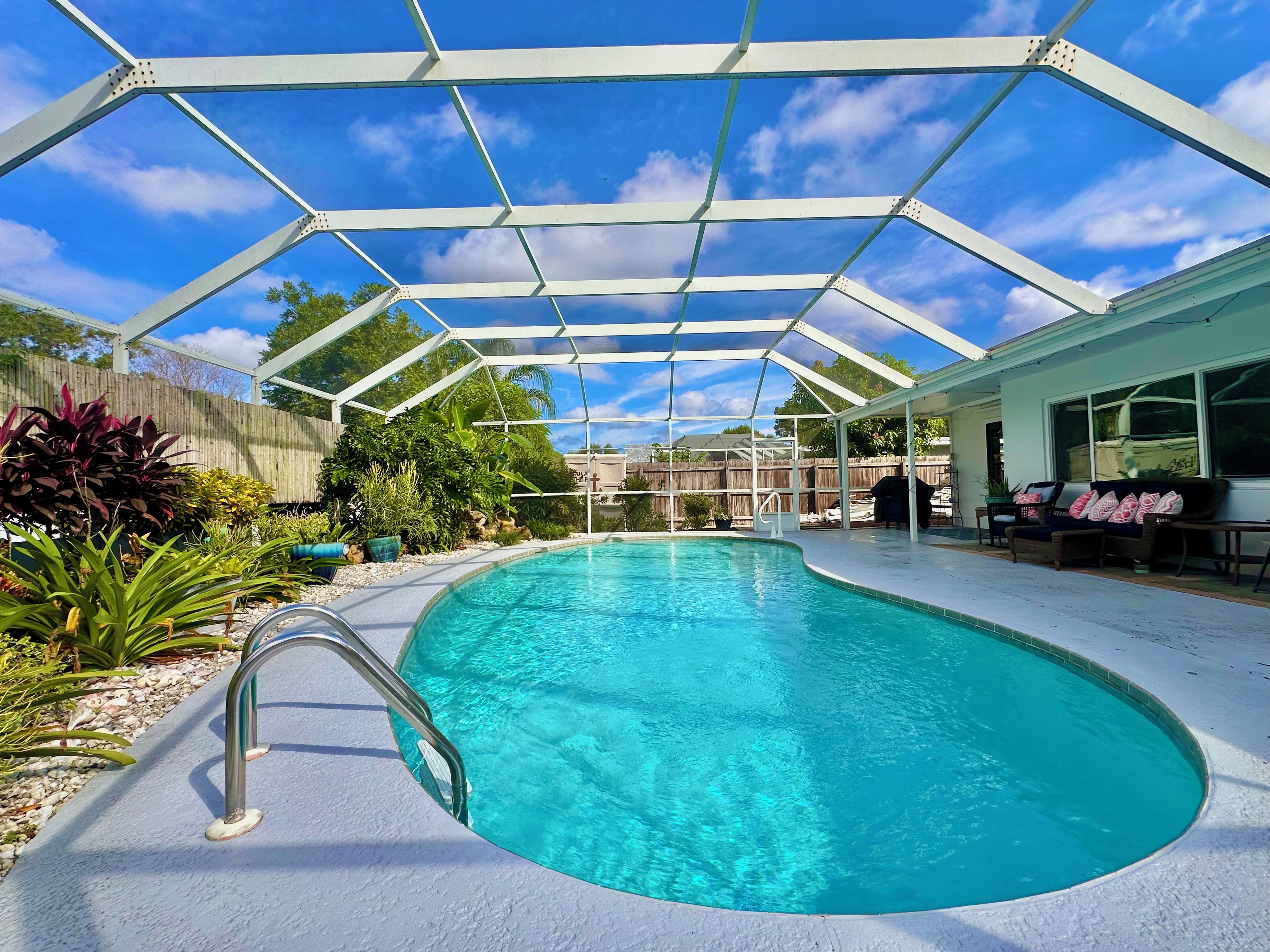 A covered swimming pool with a metal frame, surrounded by plants and a wooden fence.