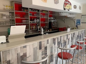 A bar area with shelves stocked with bottles and glasses, a cash register, and red bar stools. - Chalet with air conditioning - 6 guests (Saint-Maime)