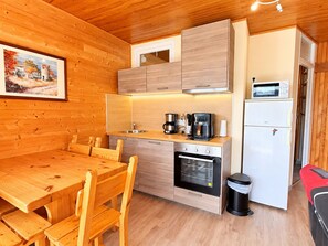 A compact kitchen with wooden cabinets, a built-in oven, a coffee maker, and a microwave. - Cozy apartment mountain view - 4 guests (Chamrousse)