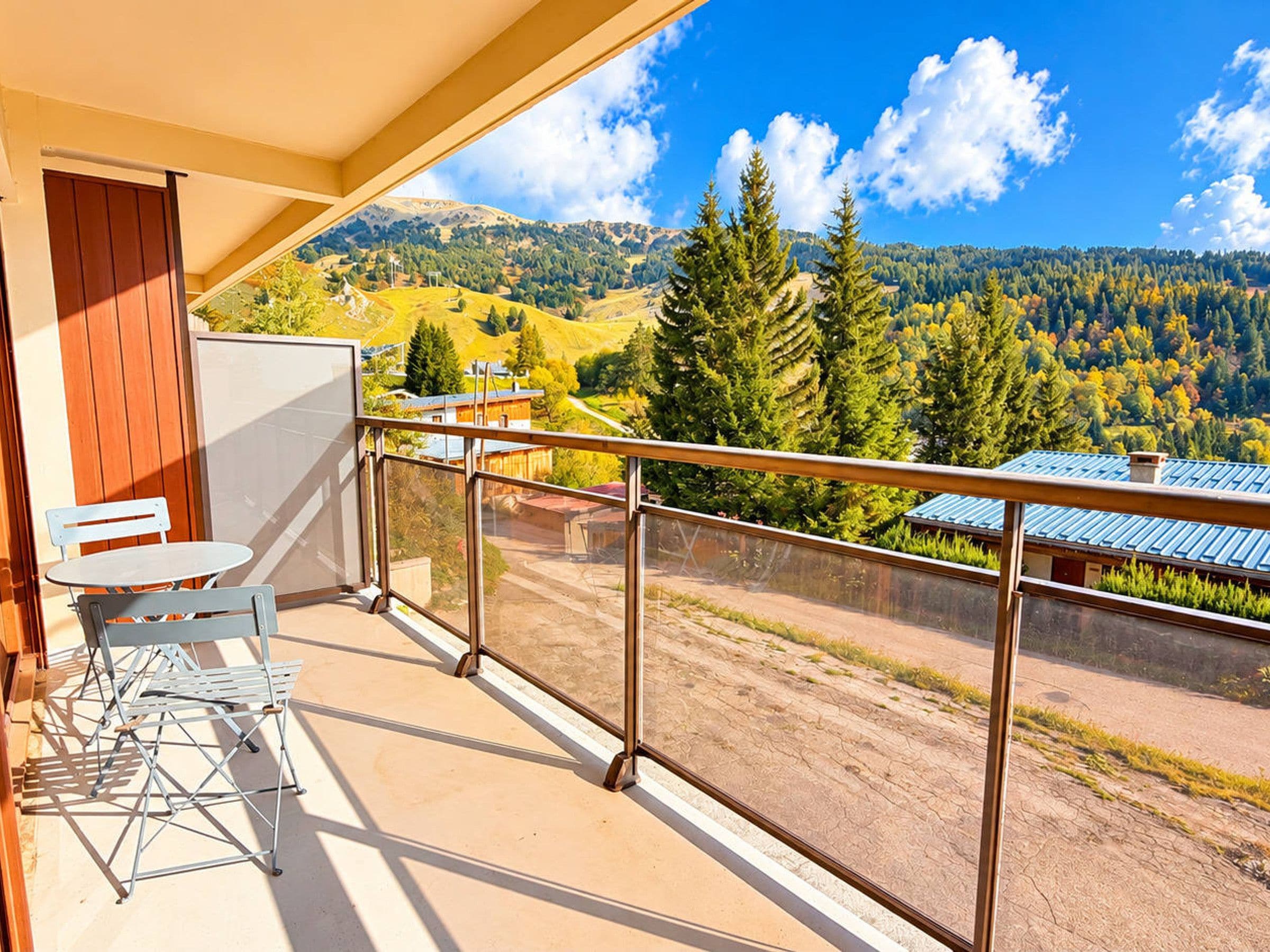 A balcony with a table and chairs, overlooking a mountainous landscape with trees and buildings.